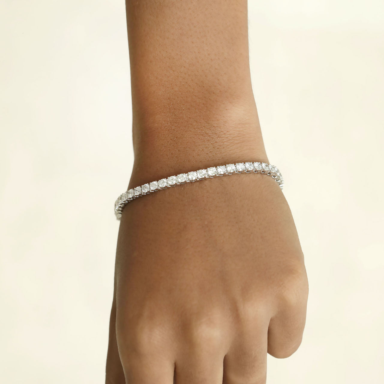Diamond bracelet on a wrist against a beige background