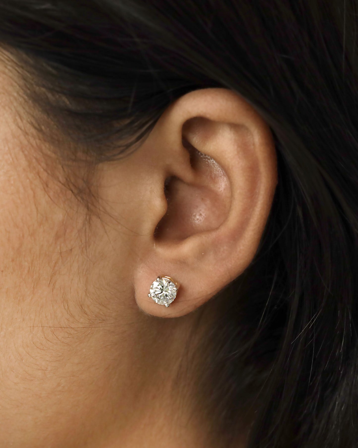 Close-up of an ear wearing a diamond stud earring with dark hair.