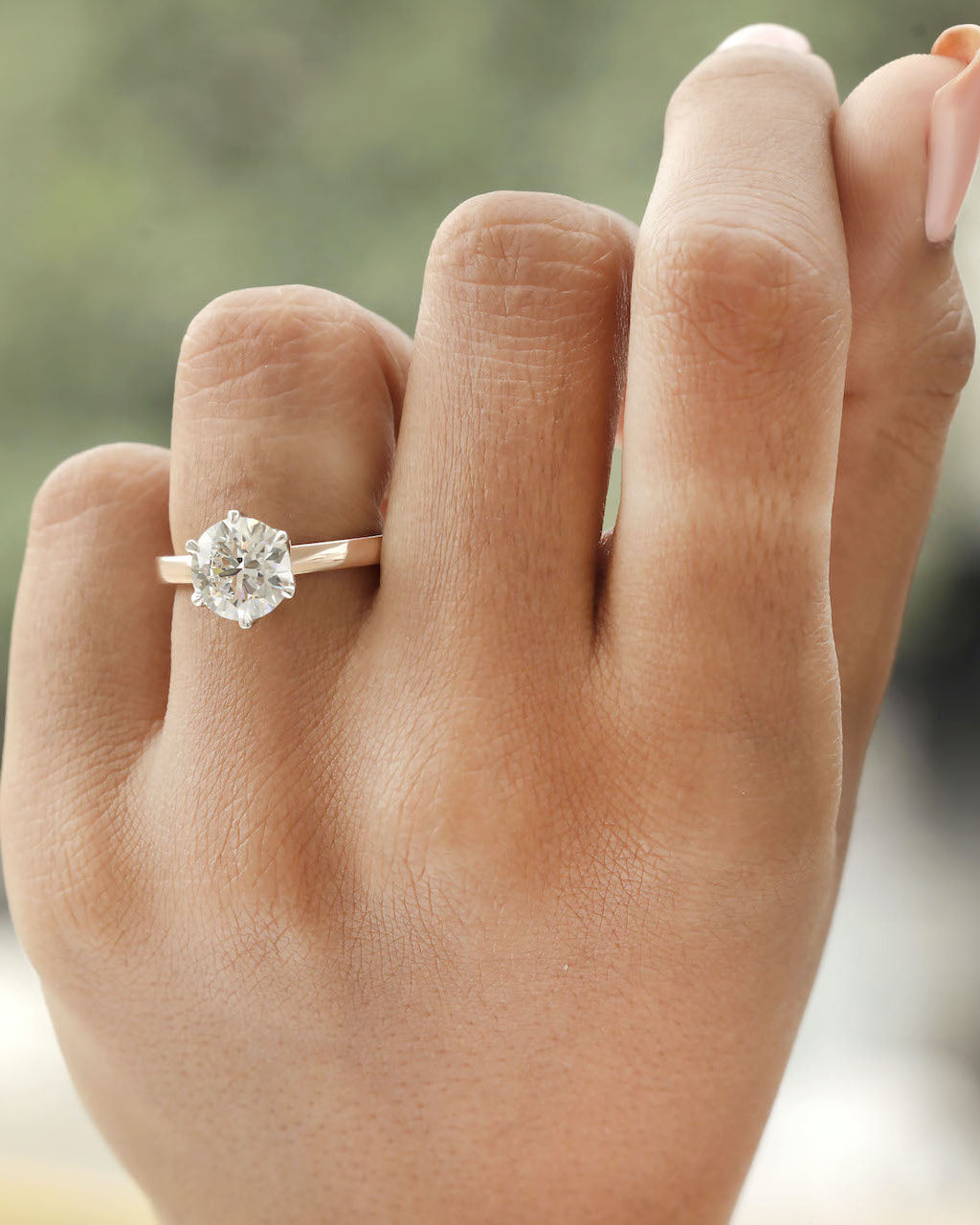 Hand wearing 2ct round brilliant engagement ring in rose gold with white gold prongs.