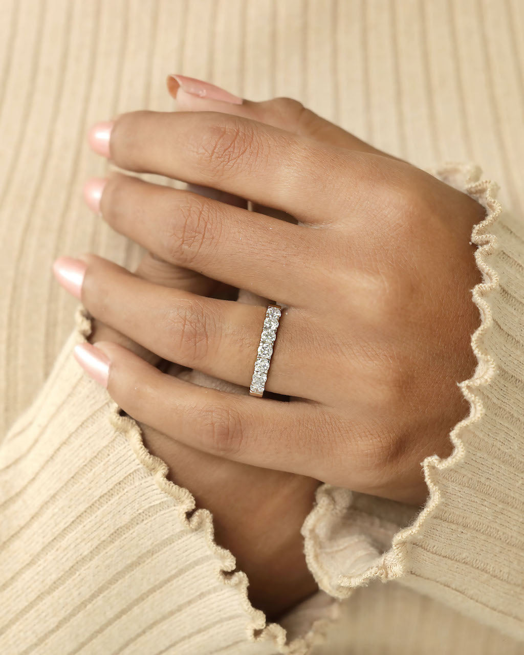 A hand wearing a half eternity diamond ring on a soft beige background.