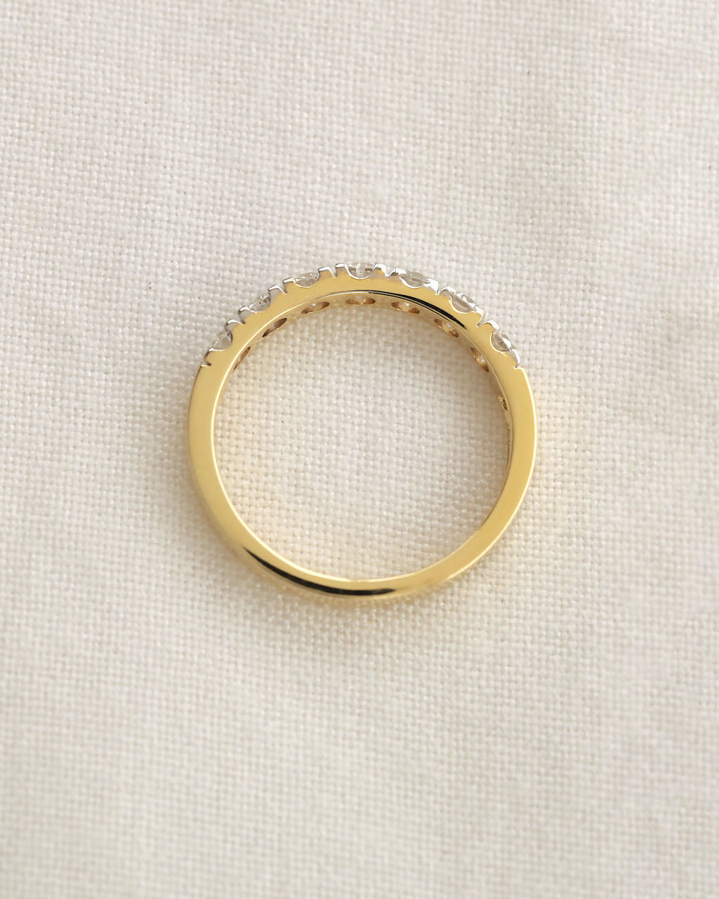 A yellow gold 7 stone half eternity diamond ring displayed on a white textured surface.