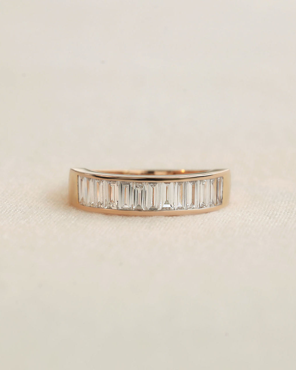 Baguette cut lab diamond eternity ring in rose gold on white background.