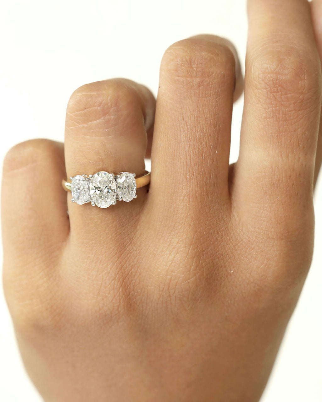 A three stone diamond ring on a hand featuring three oval cut diamonds on a yellow gold band.