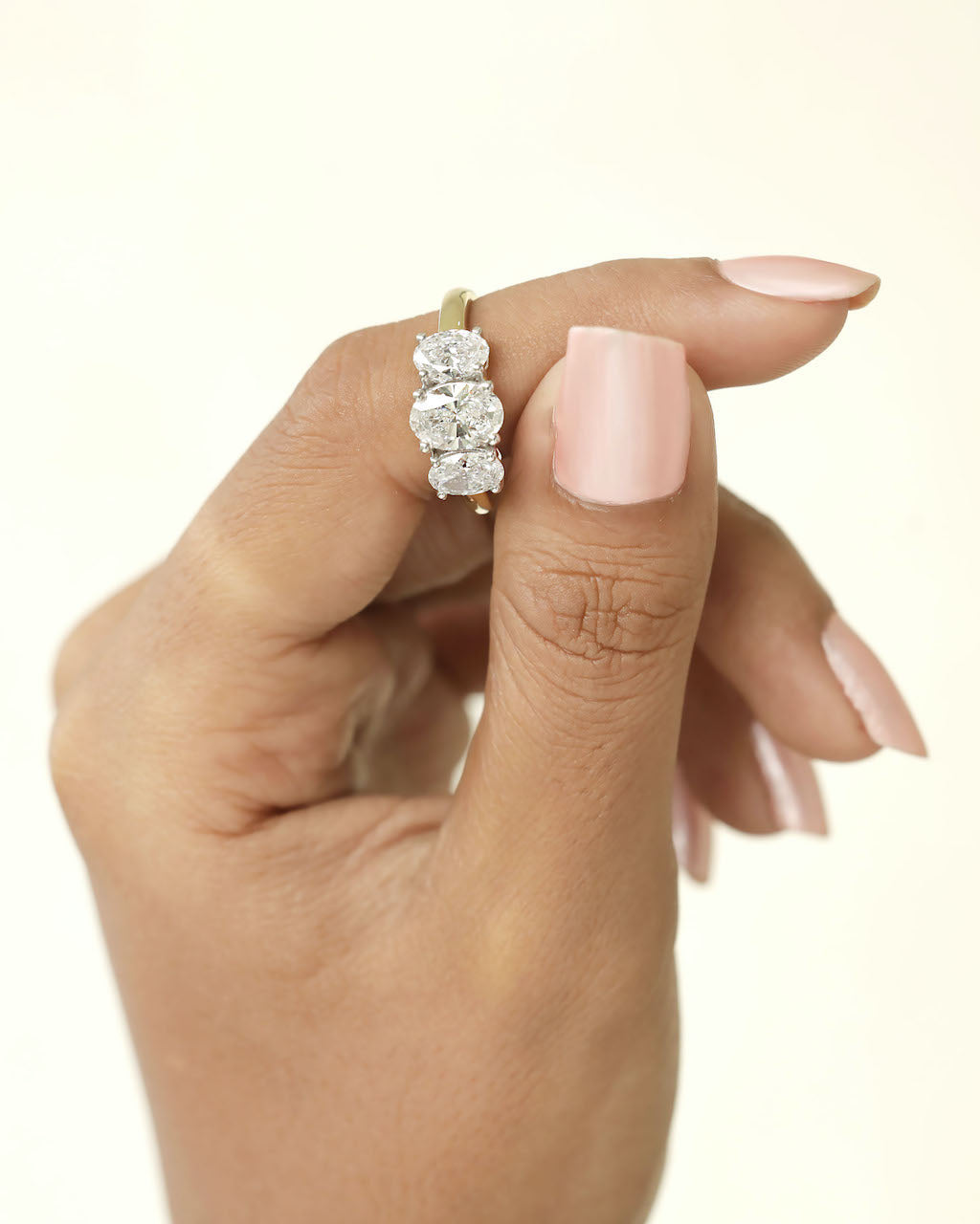 Hand holding a oval cut three stone lab grown diamond.