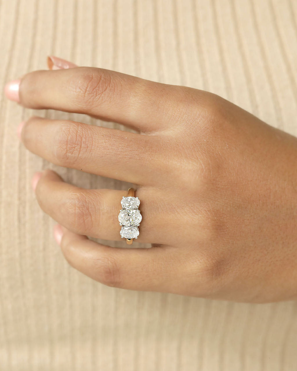 A person's hand wearing a three stone ring with oval cut diamonds.