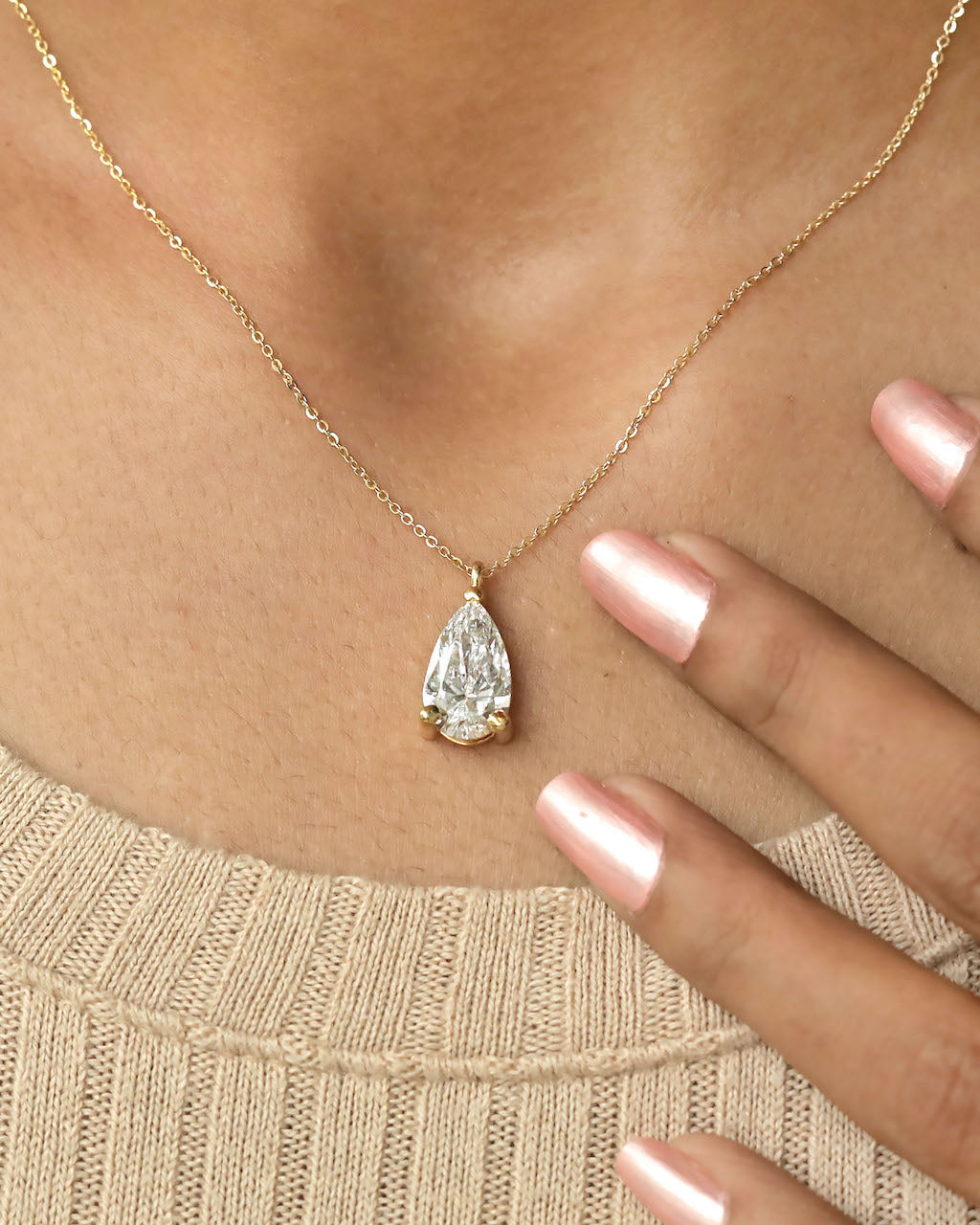 Close up shot of a person wearing pear cut lab diamond solitaire pendant necklace in yellow gold.