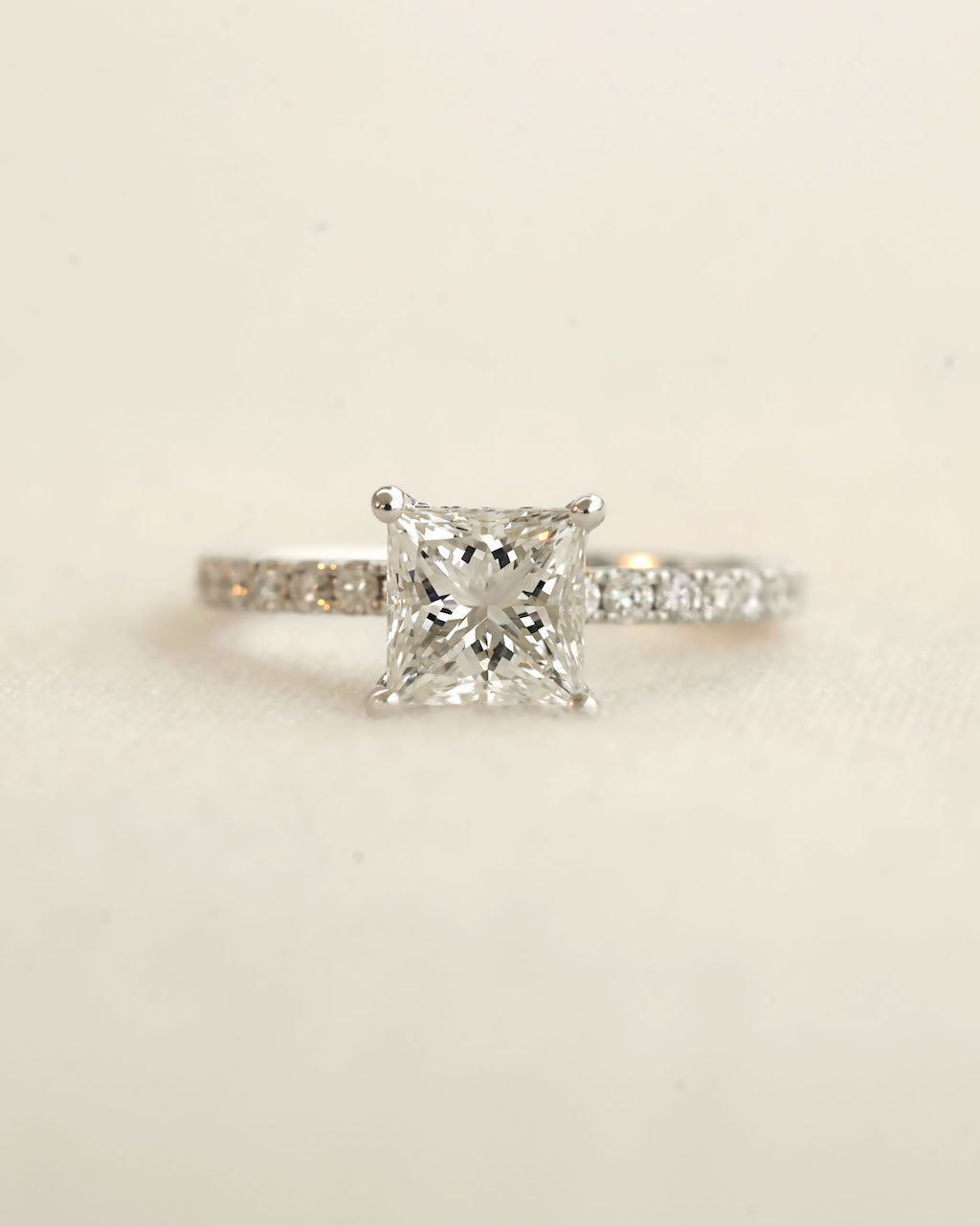Close up shot of princess cut diamond engagement ring displayed on a white background.