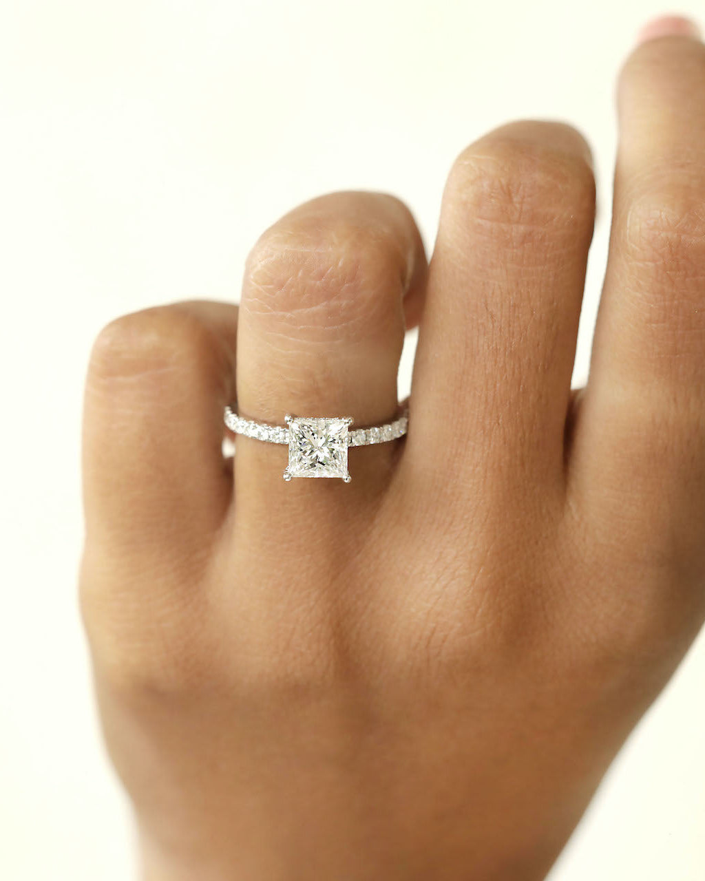 Close up shot of hand wearing a Princess cut diamond ring on a white background.