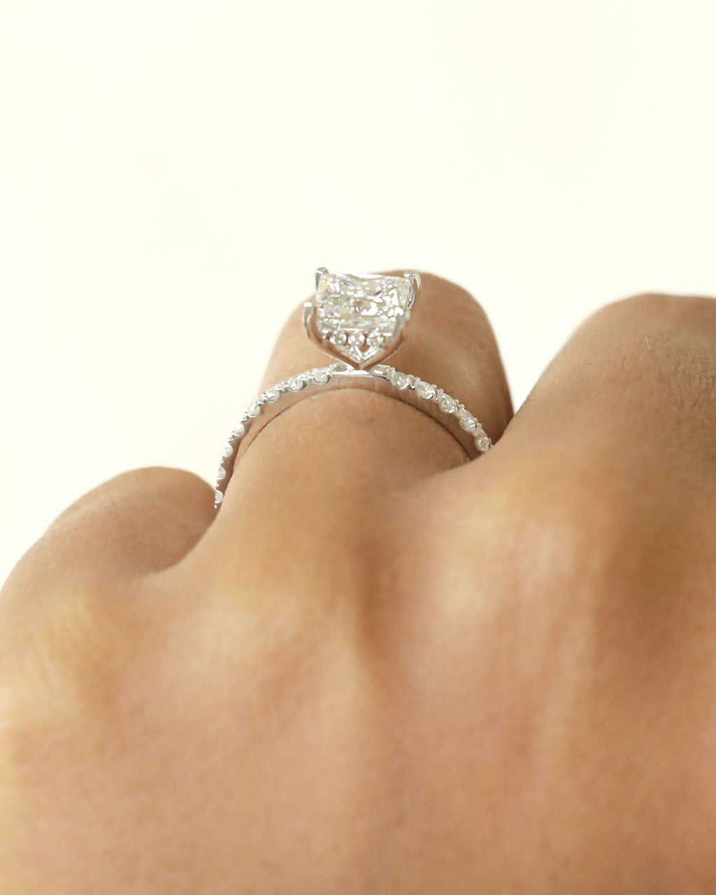 Close up shot of hand wearing a Princess cut diamond ring on a white background.
