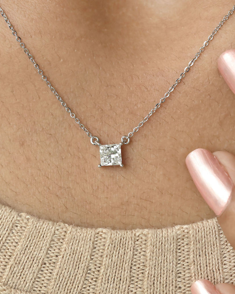 Person wearing princess cut lab diamond solitaire pendant necklace in yellow gold.