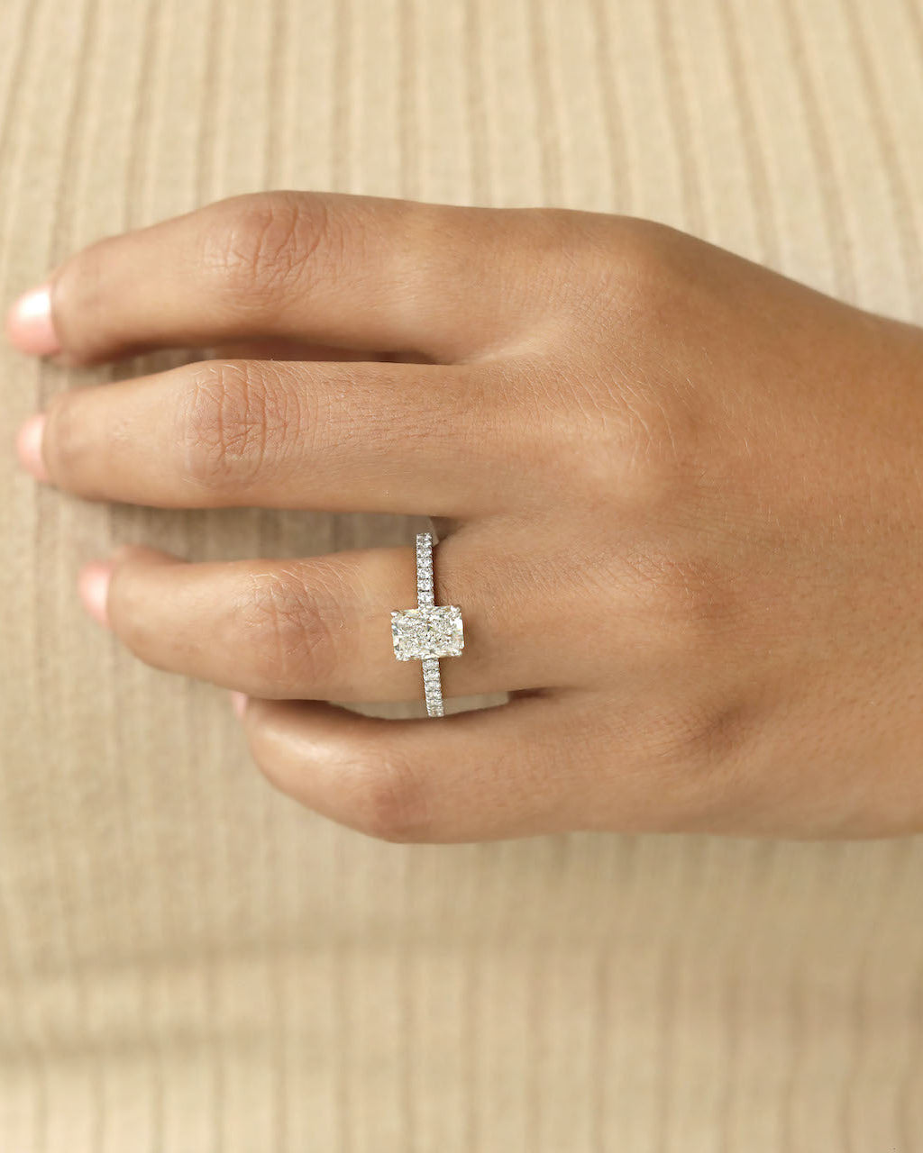 Hand wearing a diamond ring on beige background