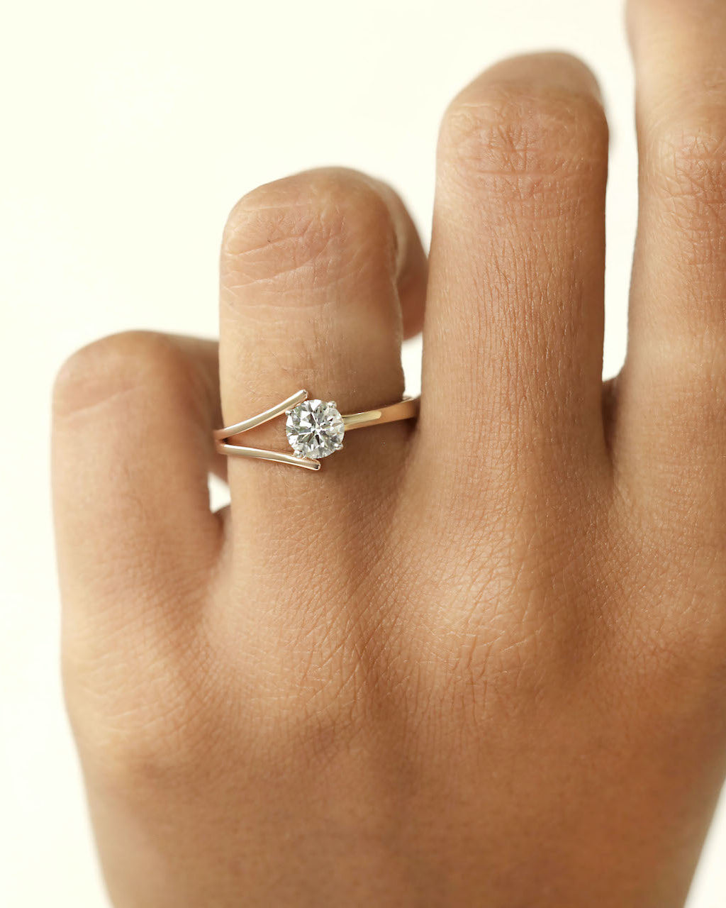 Hand wearing round cut diamond ring with modern split v band in yellow & rose gold.