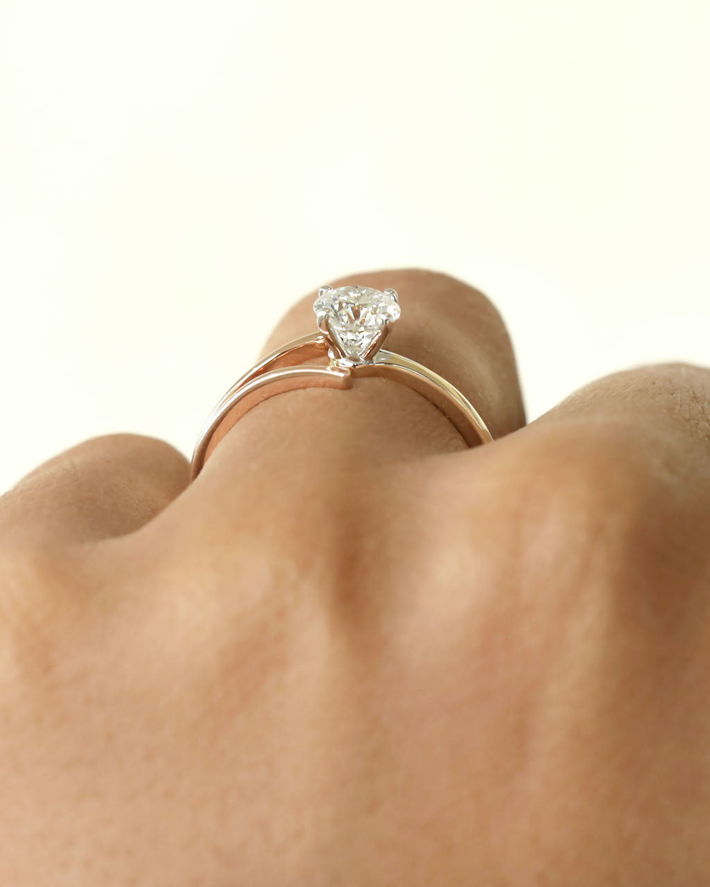 Hand wearing round cut diamond ring with modern split v band in yellow & rose gold.