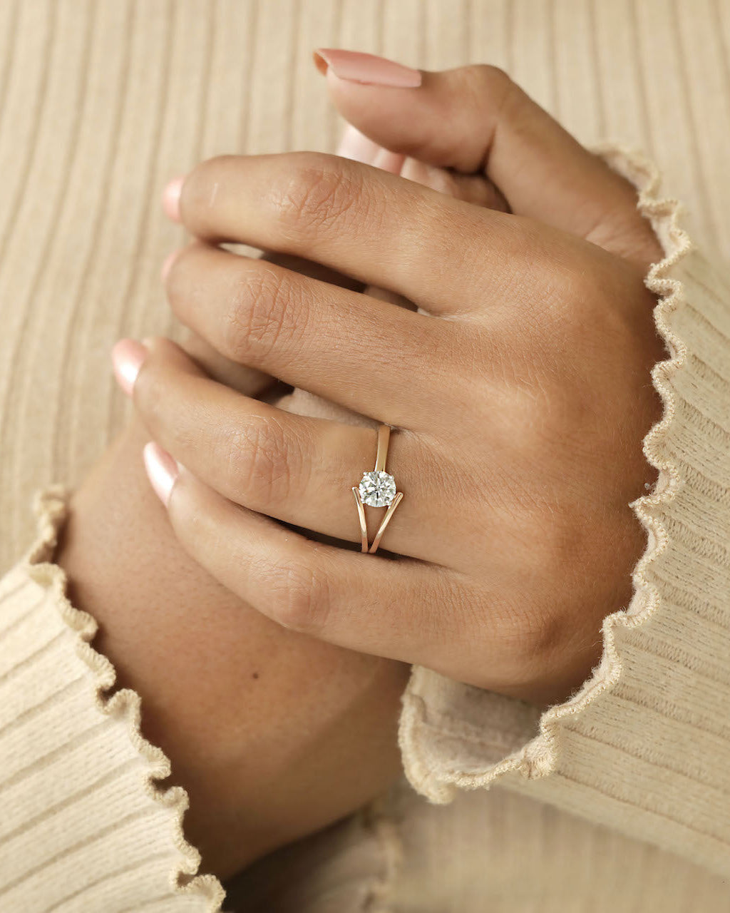 Hand wearing round cut diamond ring with modern split v band in yellow & rose gold .