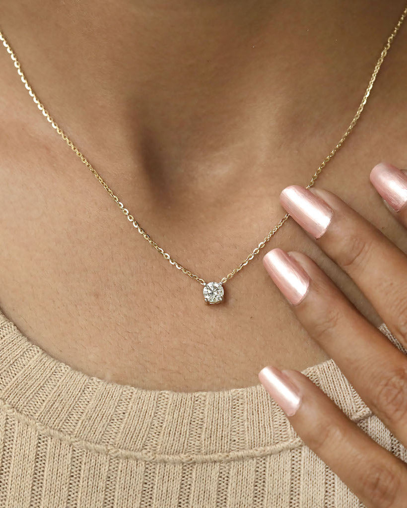Person wearing round cut lab diamond solitaire pendant necklace in yellow gold.
