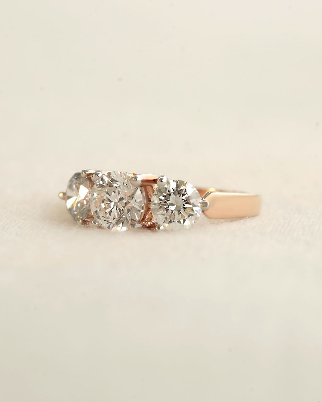 Side view of a three stone diamond ring with rose gold band displayed on white background.