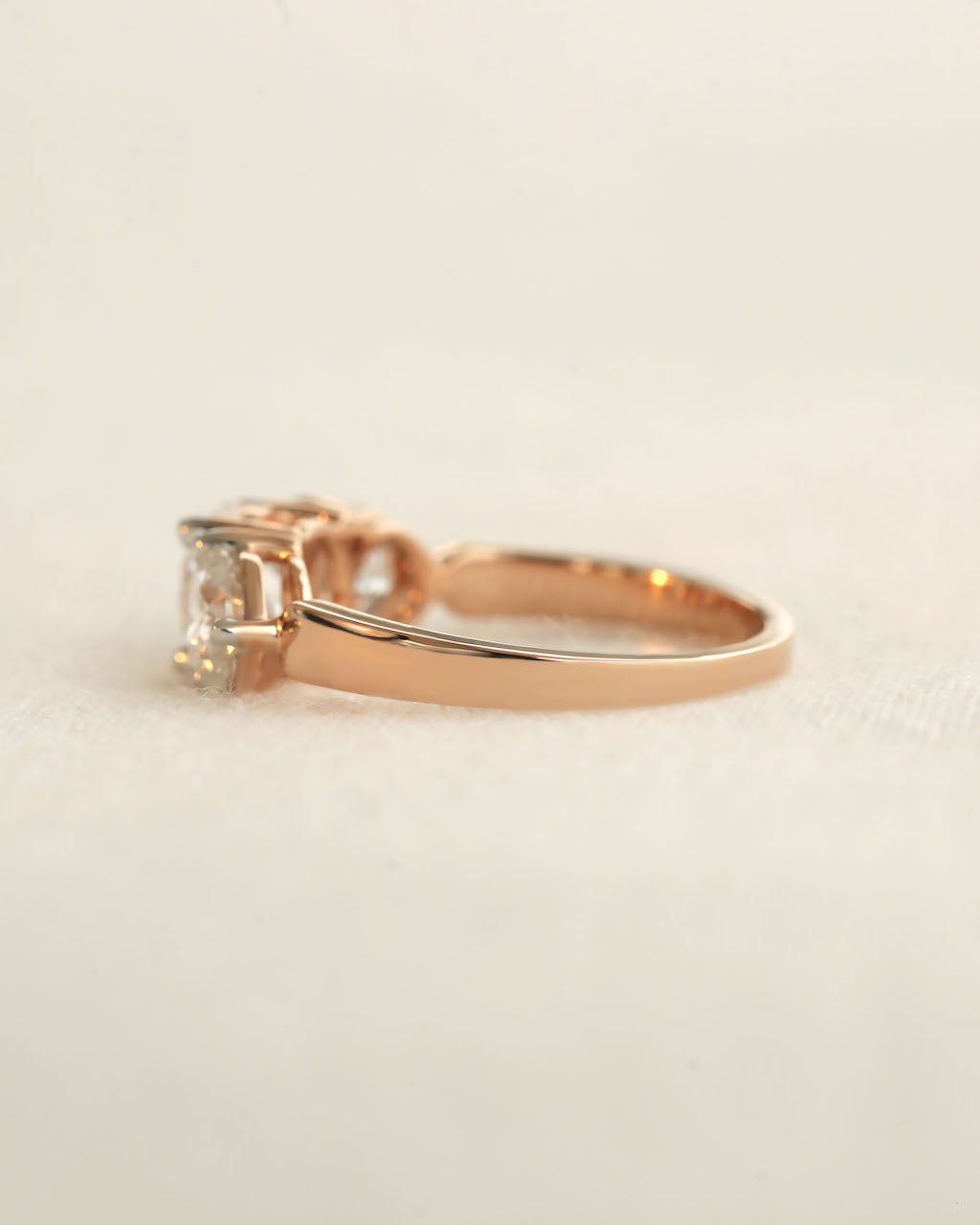 Side view of a three stone diamond ring with rose gold band displayed on white background.