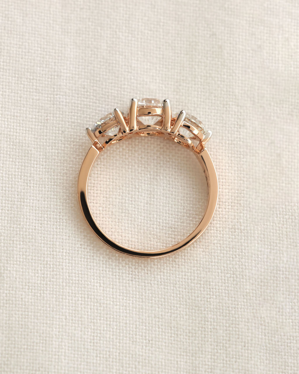 Close up shot of a three stone diamond ring with rose gold band displayed on white background.