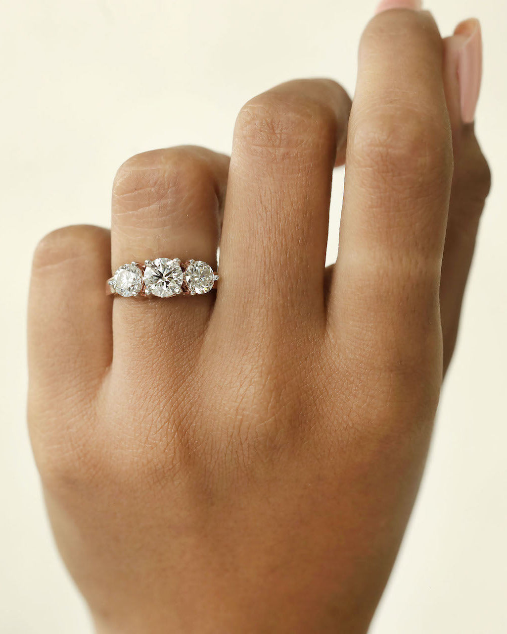 Close up shot of a hand wearing a three stone diamond ring with rose gold band .