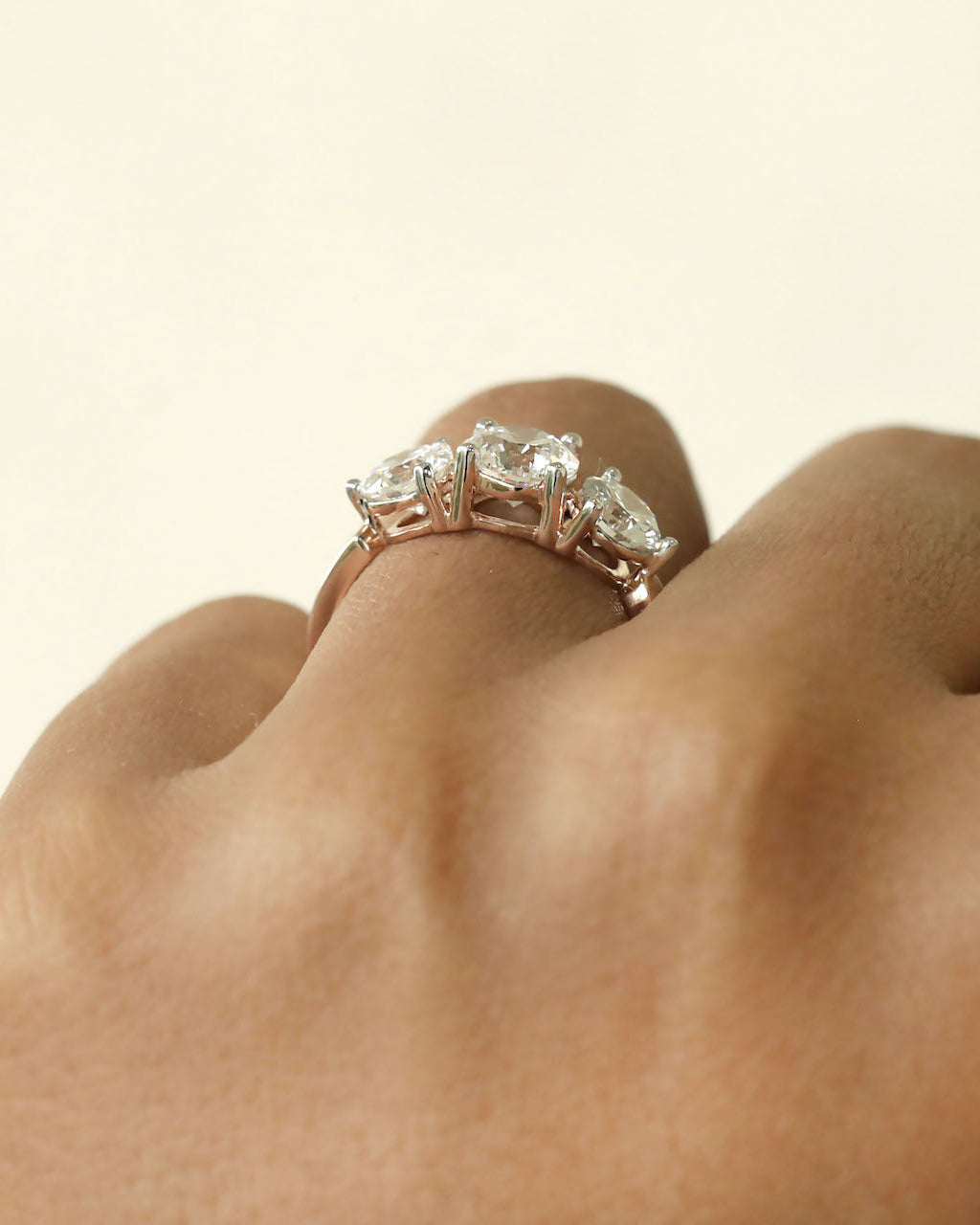 Close up shot of a hand wearing a three stone diamond ring with rose gold band .