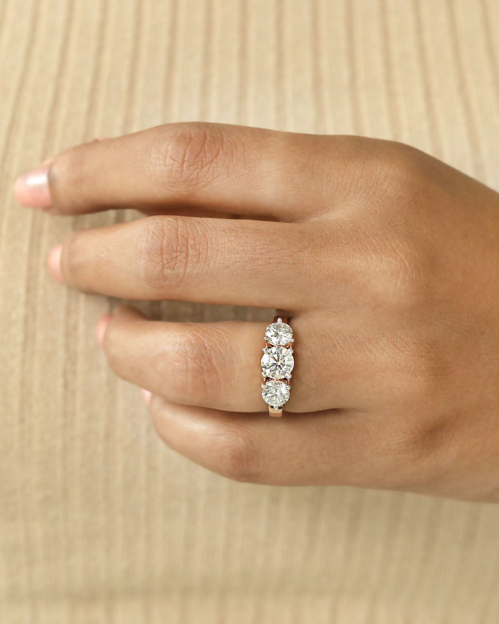 Close up shot of a hand wearing a three stone diamond ring with rose gold band .