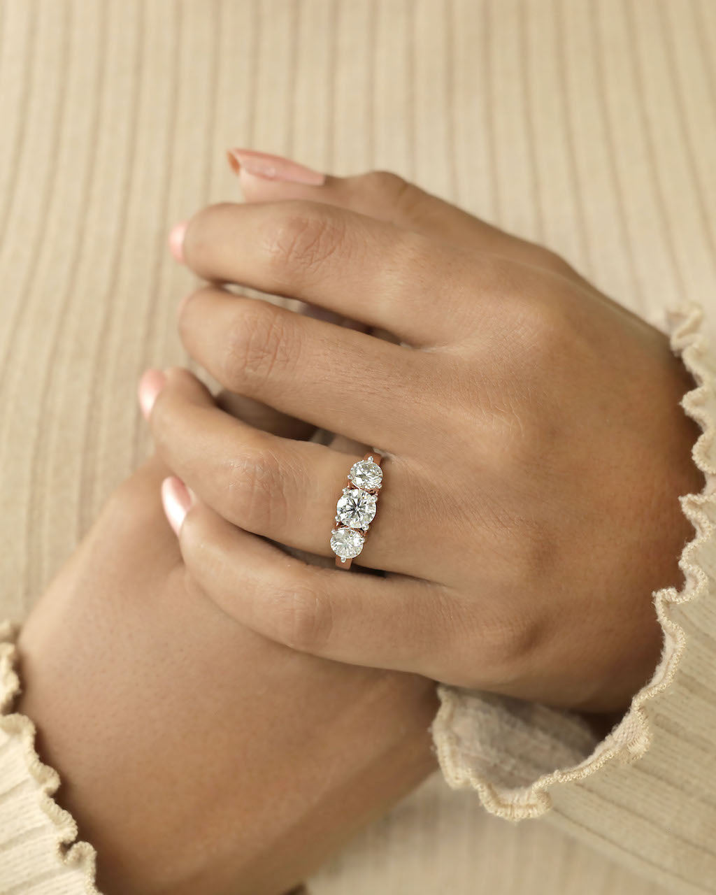 Close up shot of a hand wearing a three stone diamond ring with rose gold band .