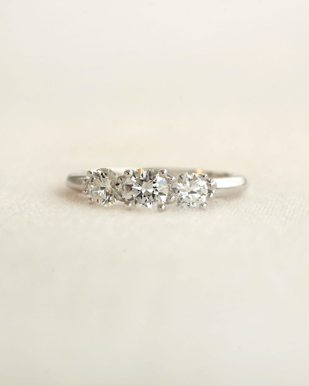 Centered shot of a three stone round cut diamond ring on a light colored background.