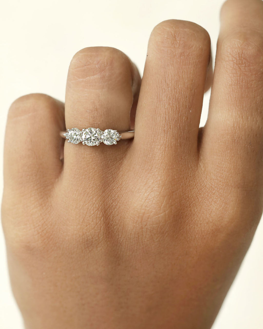 Hand wearing three stone round cut diamond ring.
