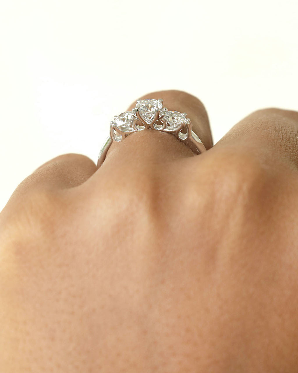 Hand wearing a three stone round cut diamond ring on the finger.