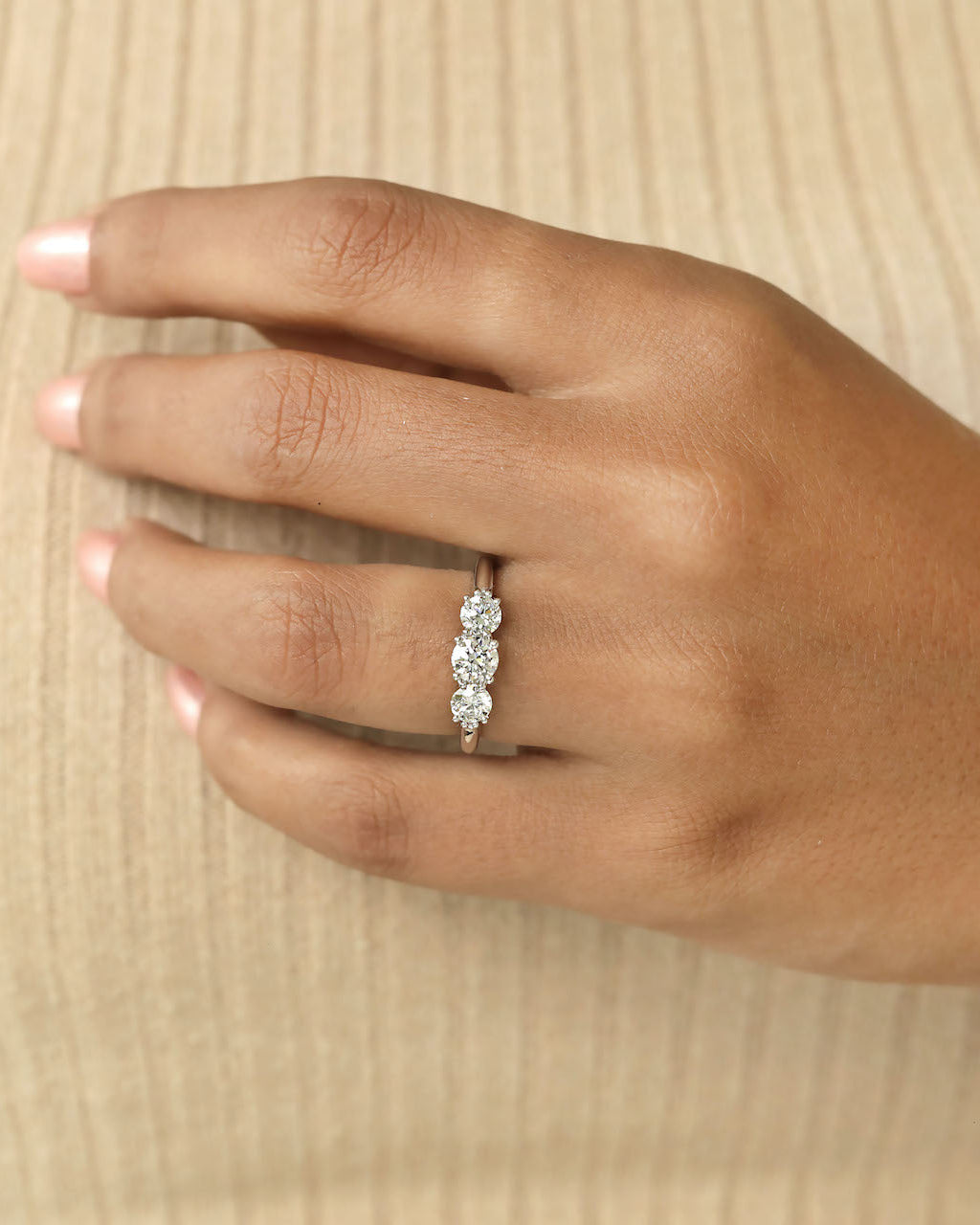Hand wearing three stone round cut diamond ring .
