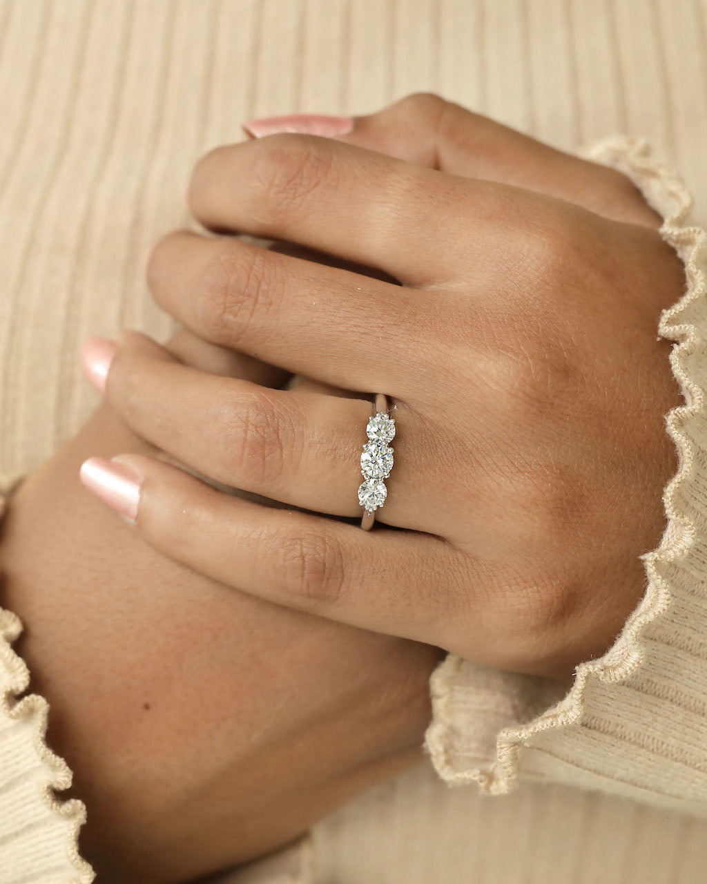 Hand wearing three stone round cut diamond ring.