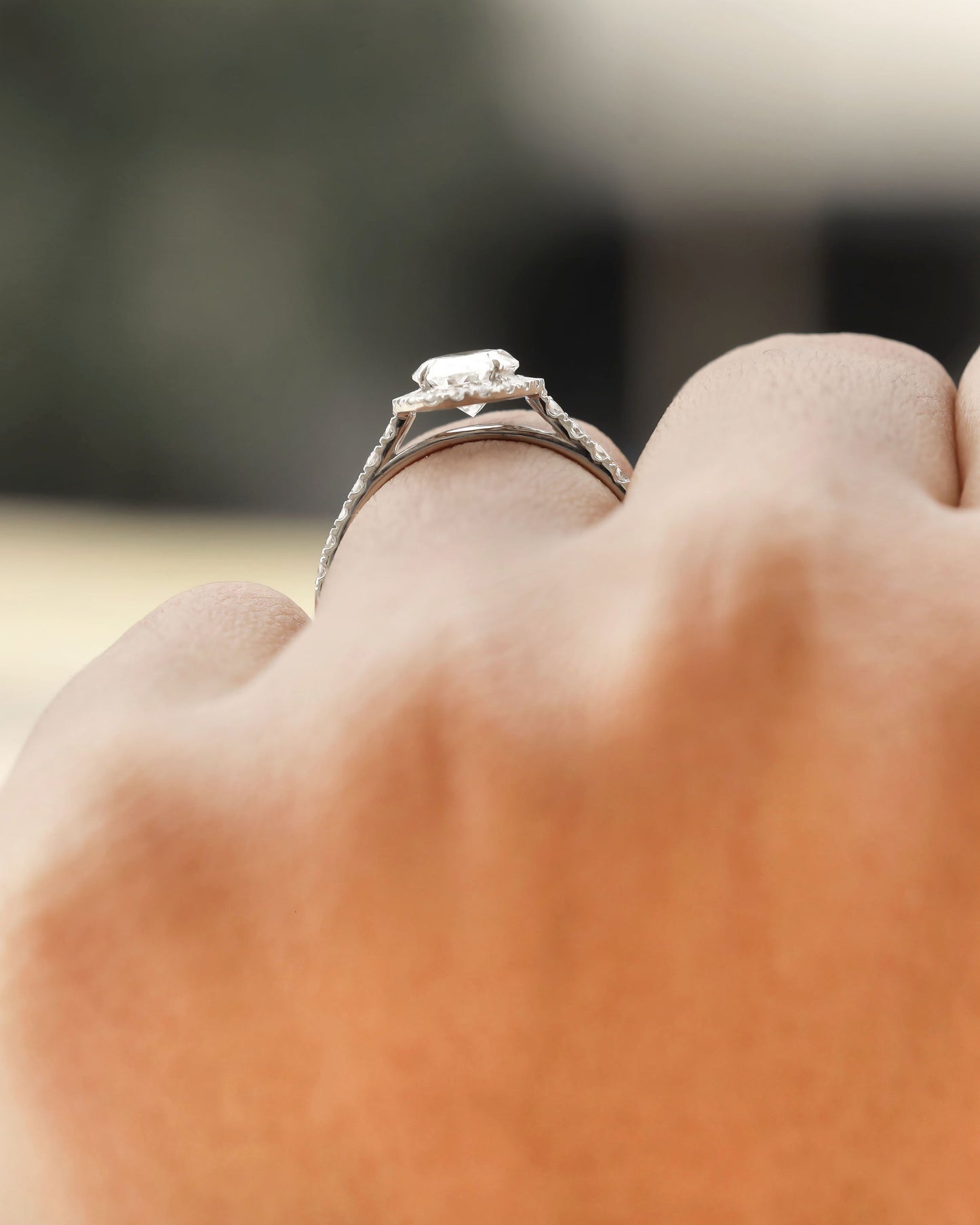 Hand wearing white gold oval halo engagement ring.