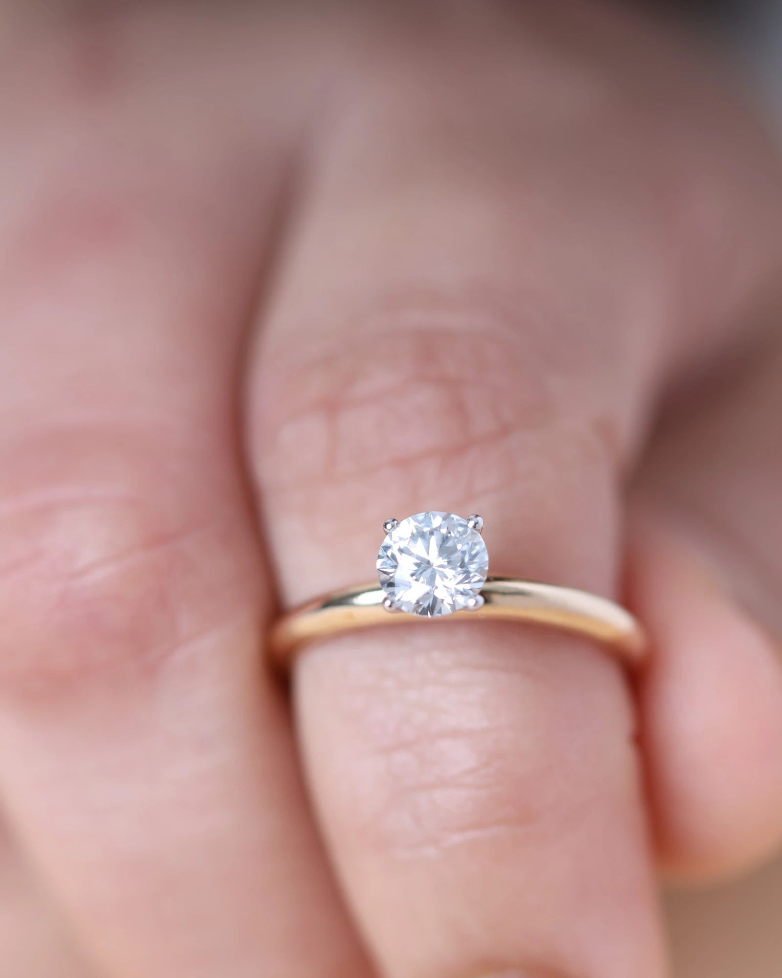 Hand wearing round brilliant diamond engagement ring.