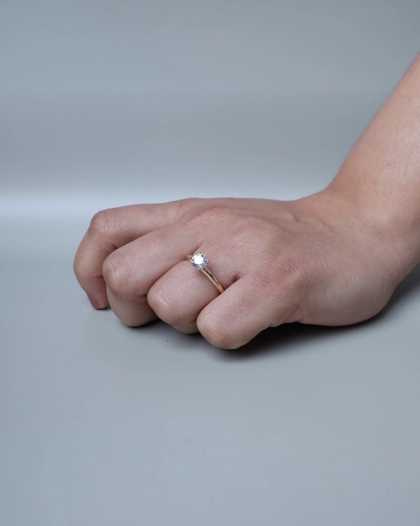 Hand wearing round brilliant diamond engagement ring.