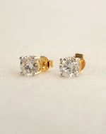 Gold diamond stud earrings on a beige background