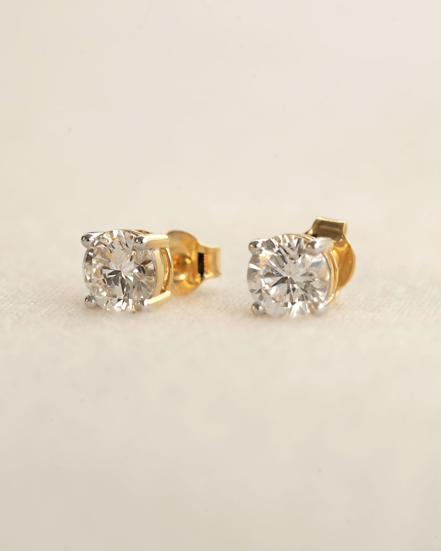 Gold diamond stud earrings on a beige background
