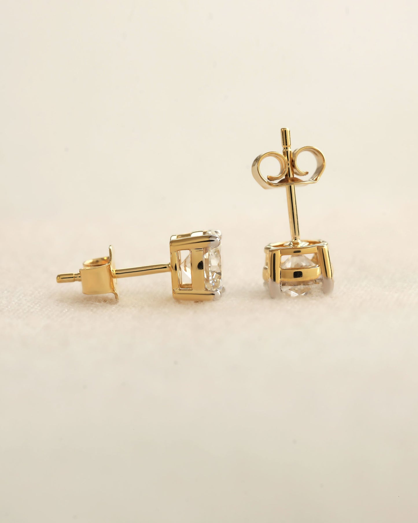 Gold stud earrings with clear gemstones on a beige background