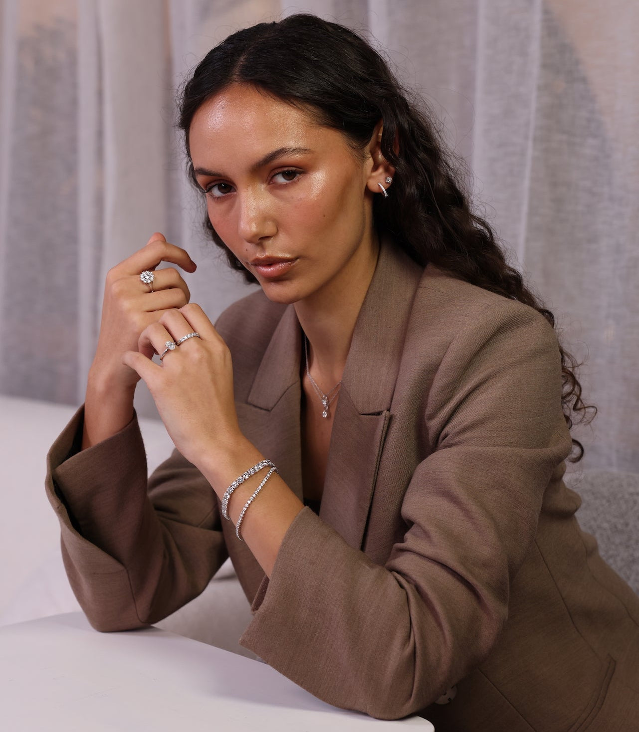 Woman wearing a brown suit with jewelry against a neutral background