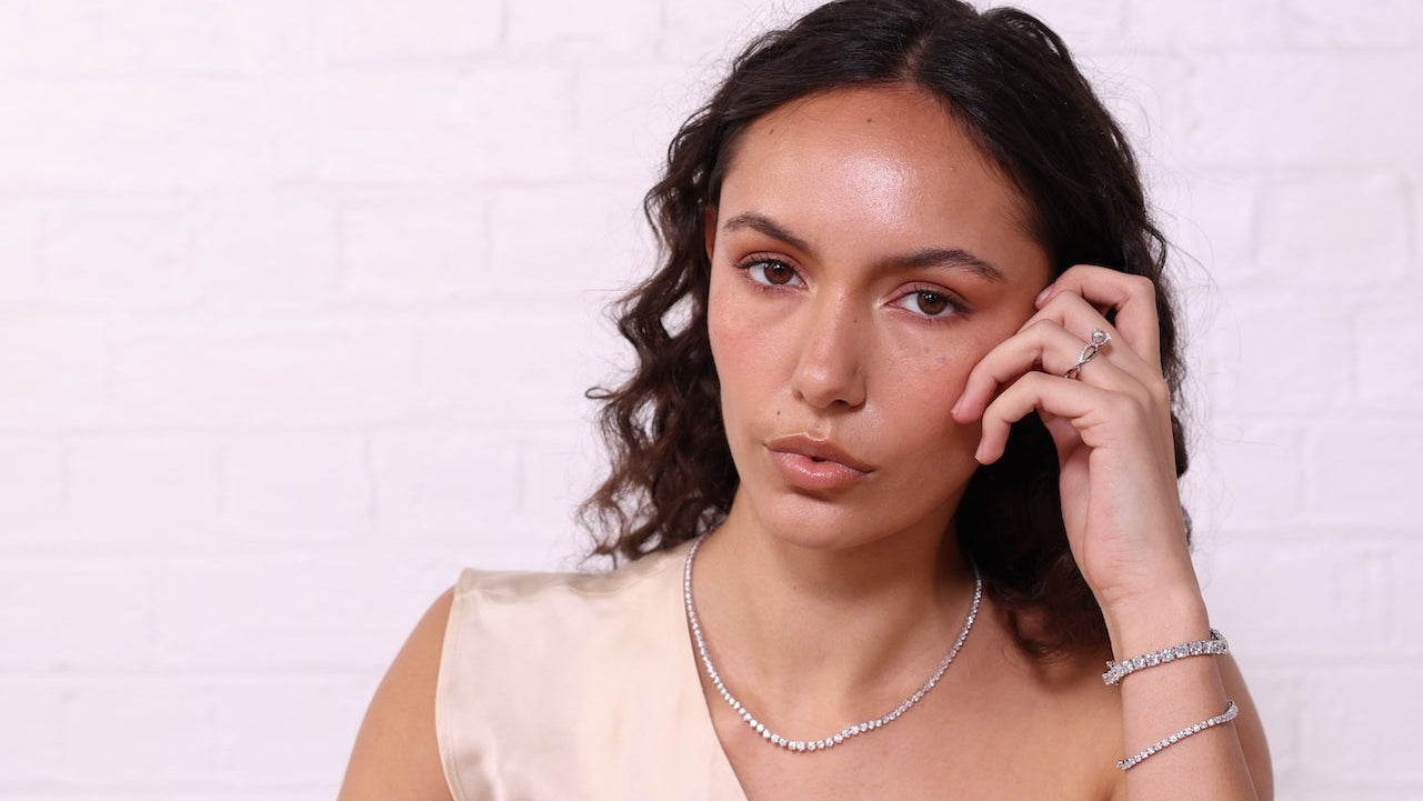 Woman wearing a beige top and jewelry against a white background