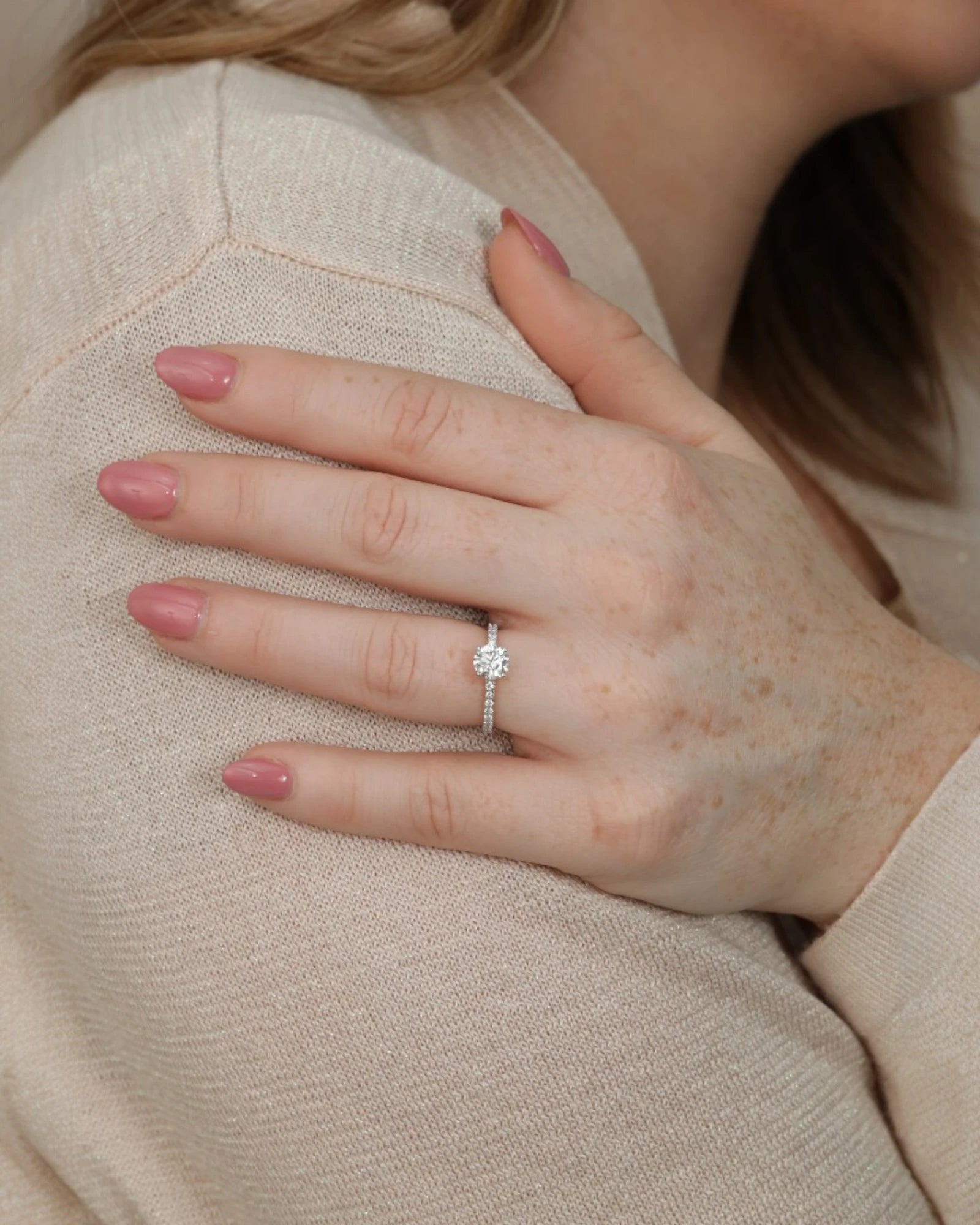 Hand wearing round diamond engagement ring with pave band.