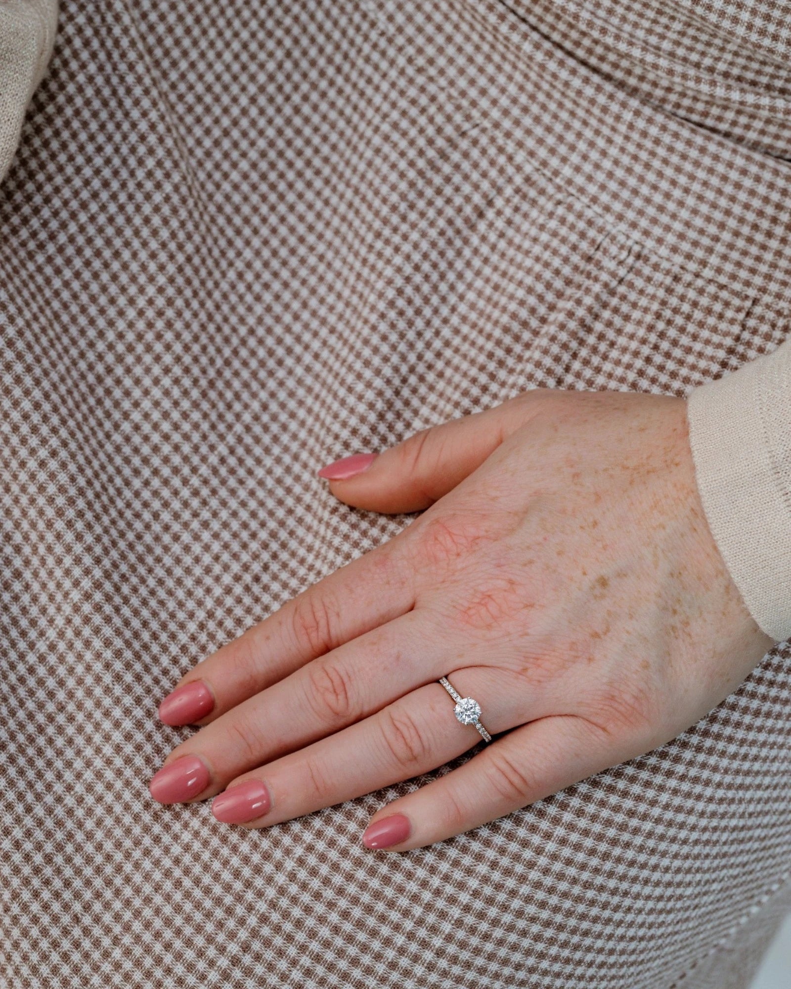Hand wearing round diamond engagement ring with pave band.