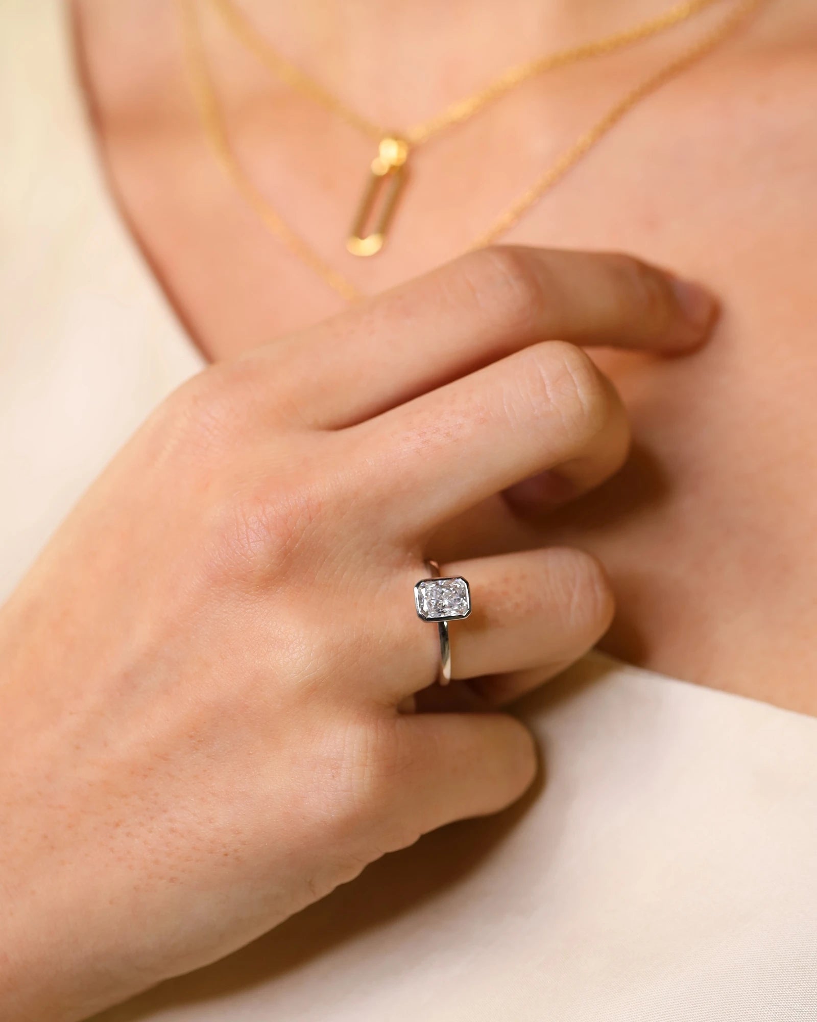 Hand wearing radiant cut diamond bezel ring in white gold.