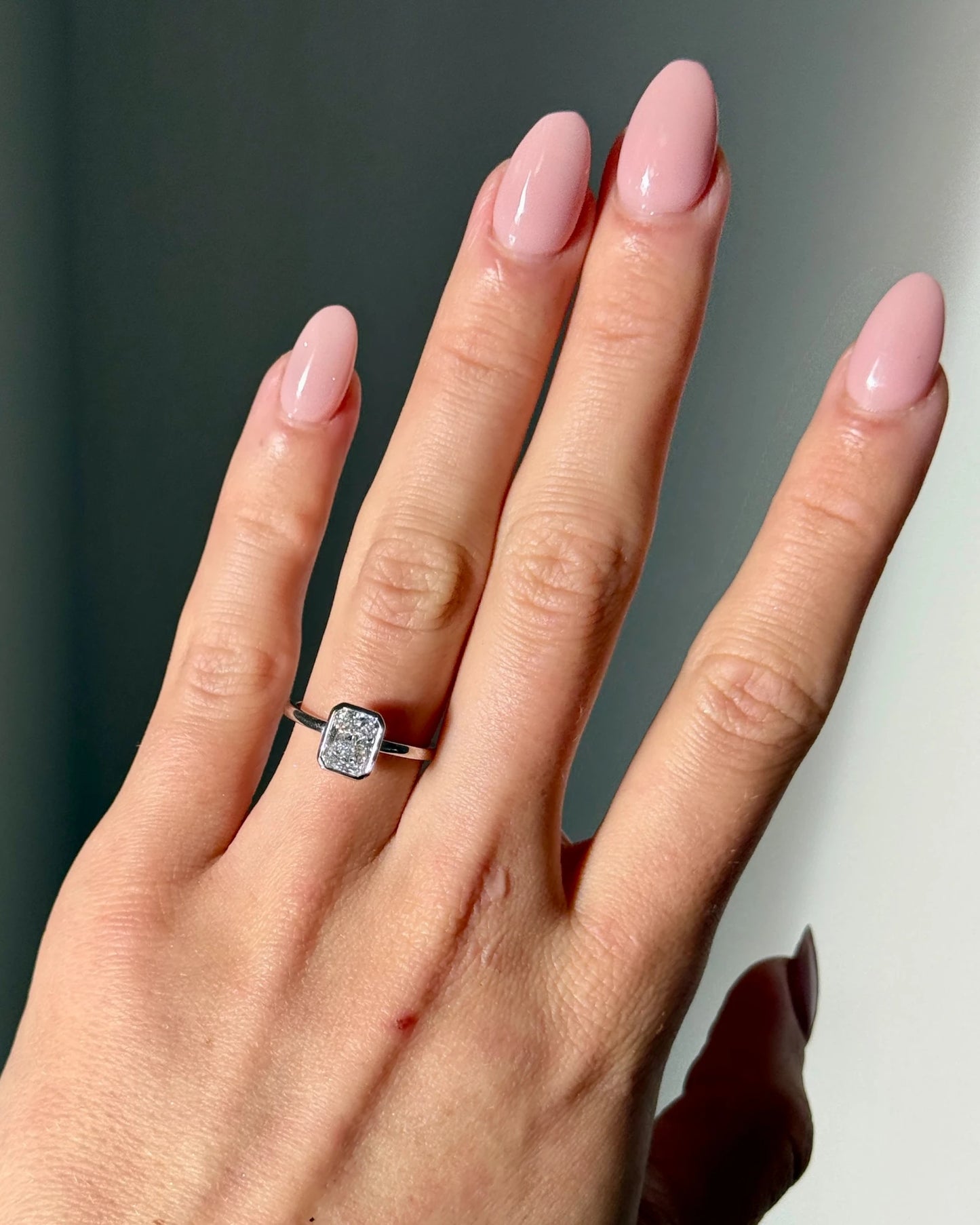 Hand wearing radiant cut diamond bezel ring in white gold.