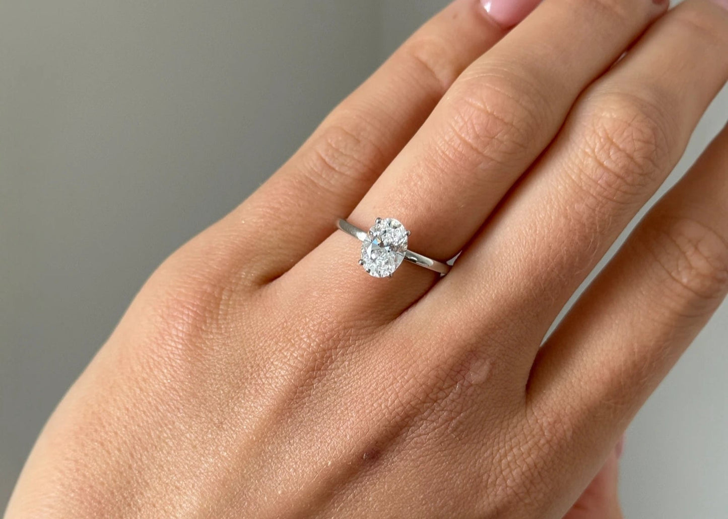 Hand wearing a diamond ring on a neutral background