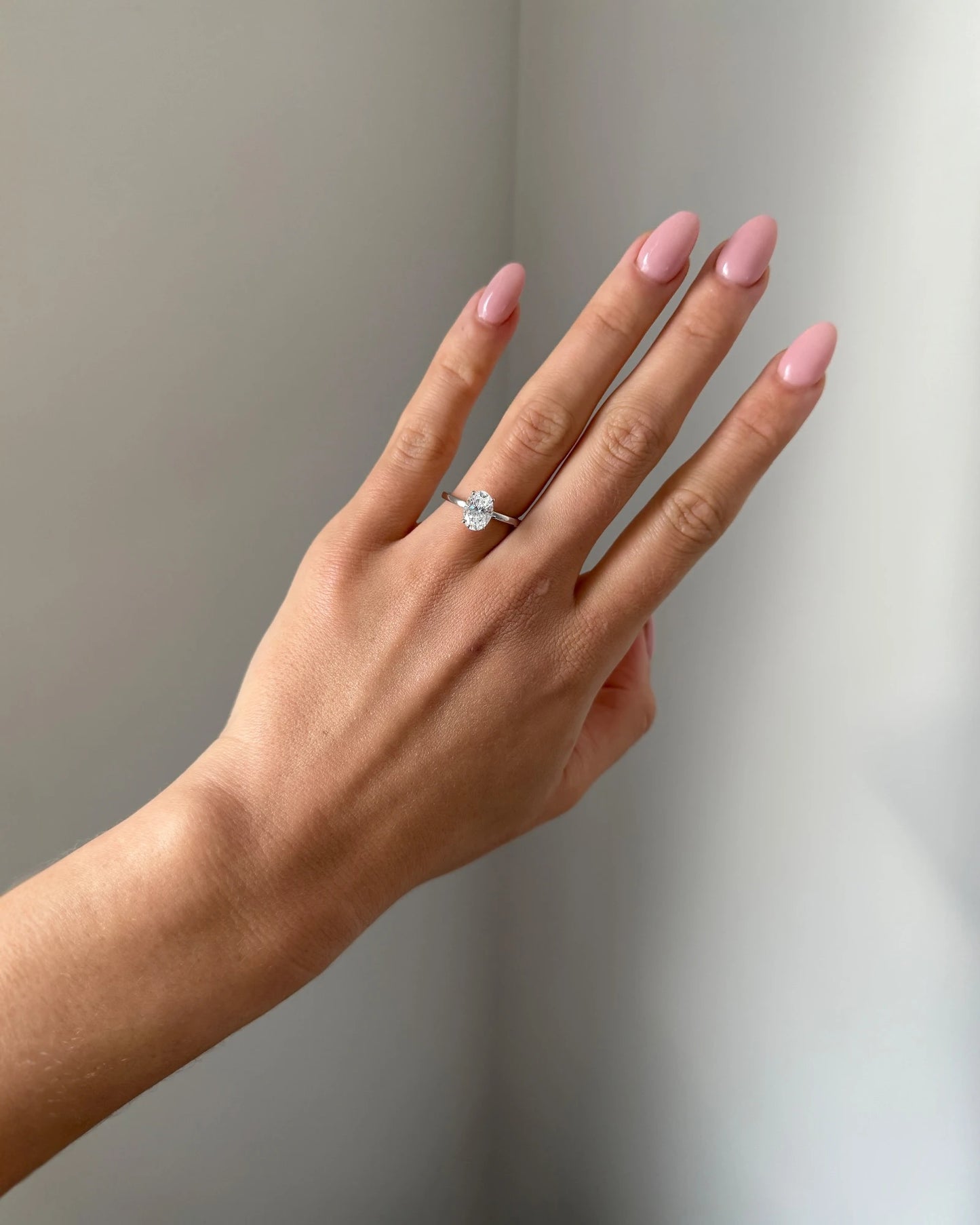 Hand wearing a diamond ring on a neutral background