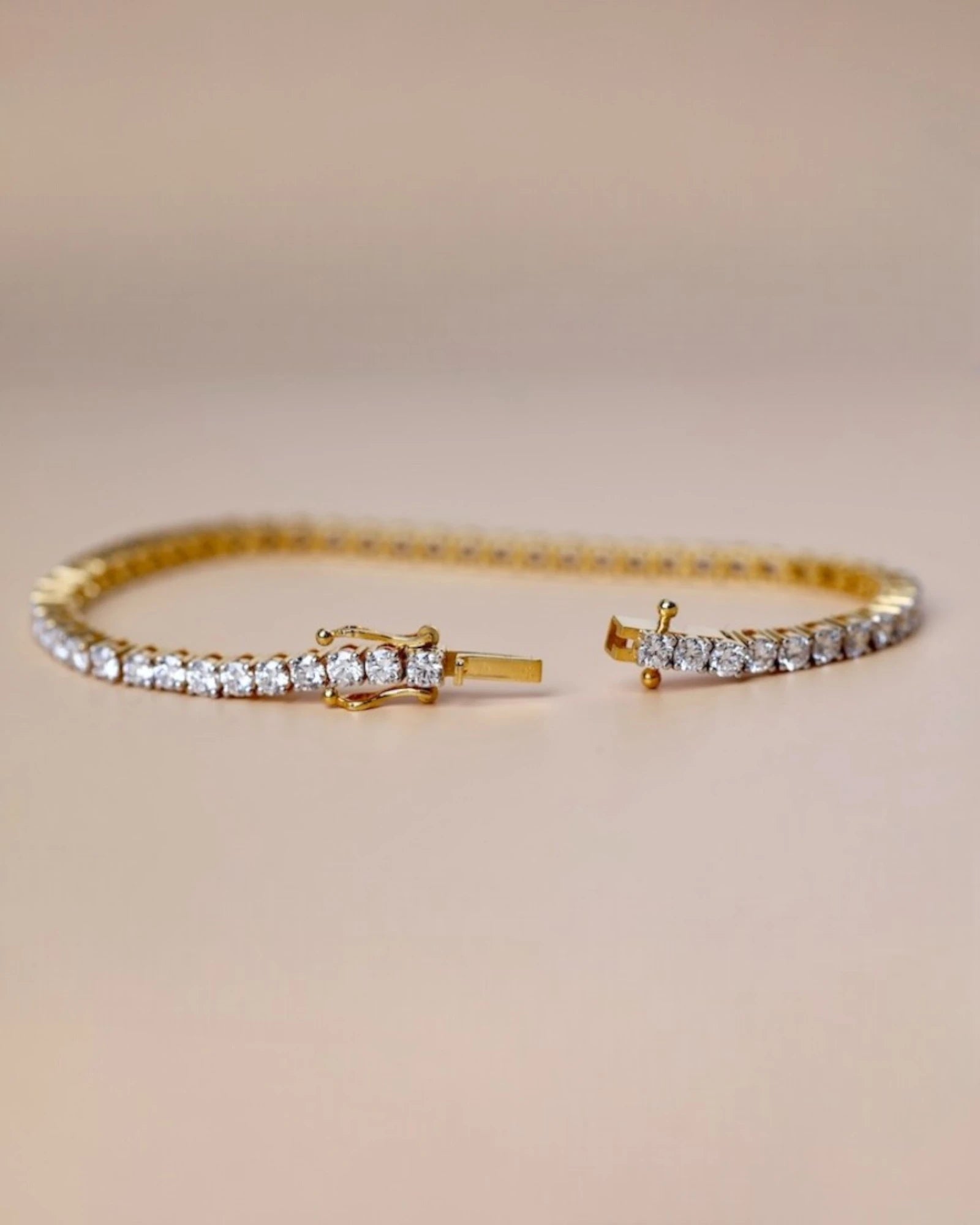 Yellow gold tennis diamond bracelet on beige background.