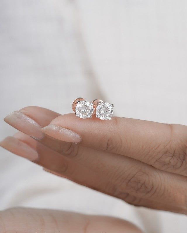 Rose gold diamond solitaire stud earrings on a hand.