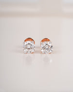 Rose gold diamond solitaire stud earrings on a white background.