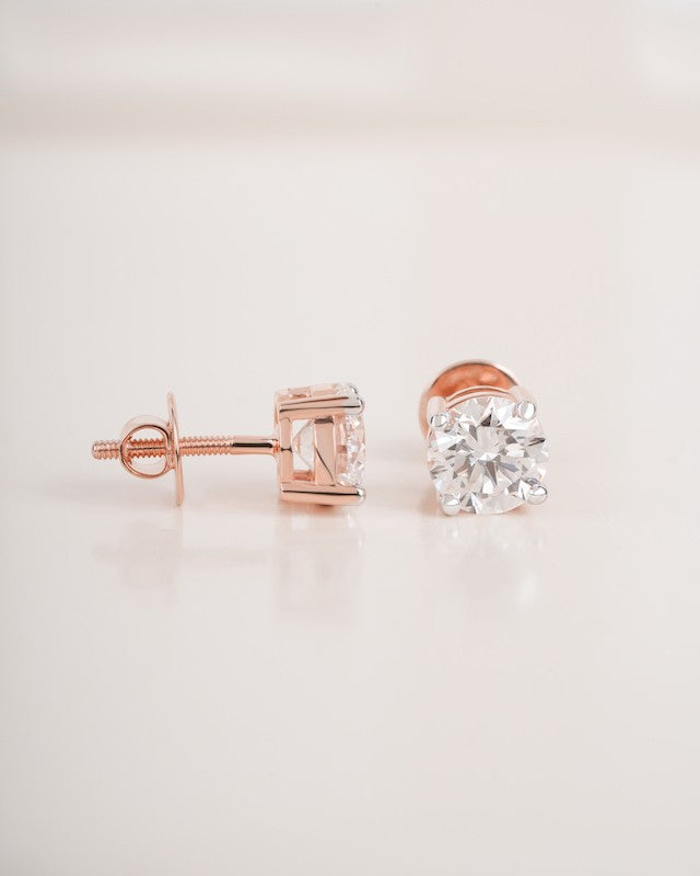Rose gold diamond solitaire stud earrings on a white background.
