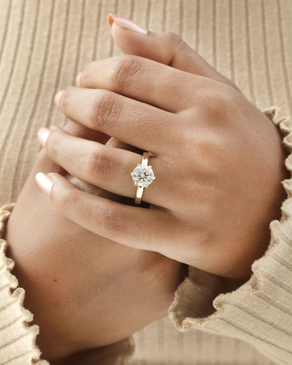 Hand wearing 2ct round brilliant engagement ring in rose gold with white gold prongs. 
